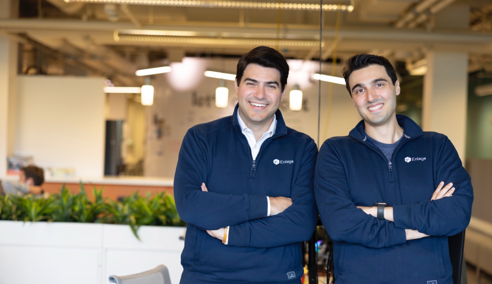 Enlaye cofounders Philippe Rival and Stamatios Liapis, arms crossed, in Enlaye jumpers in an open-plan office